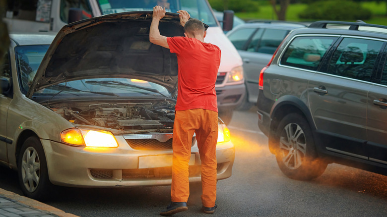 A photo of a man standing beside a broken down car