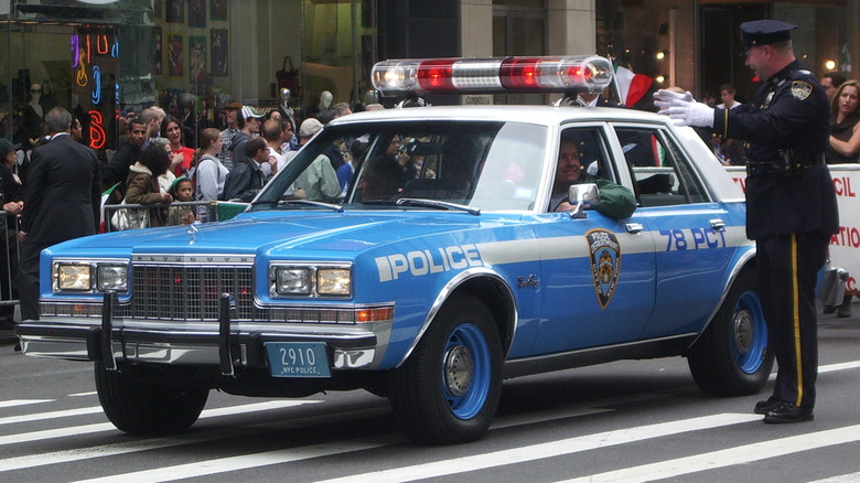 A blue-and-white Plymouth Gran Fury police car standing in a city street.
