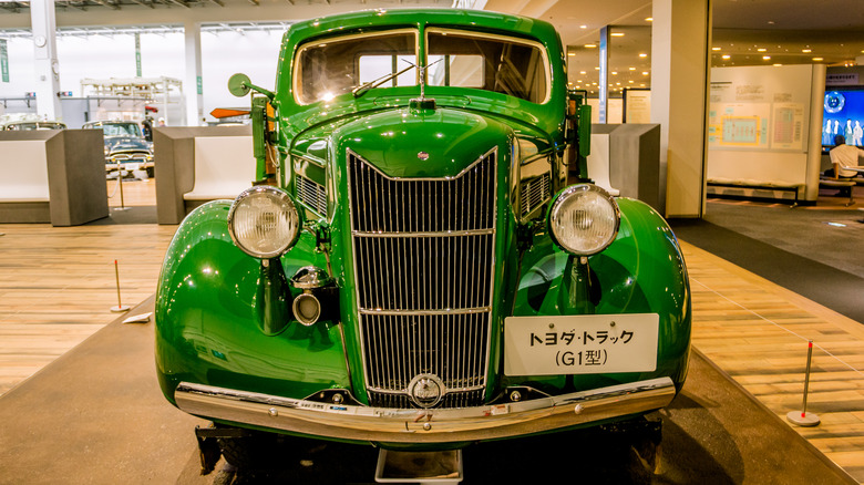 A green Toyoda Model G1 in a showroom with a Japanese sign on its front