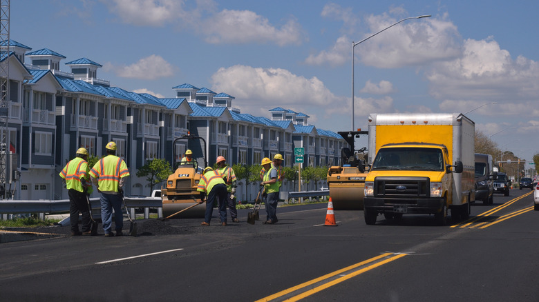 Road crew laying asphalt on busy street with traffic
