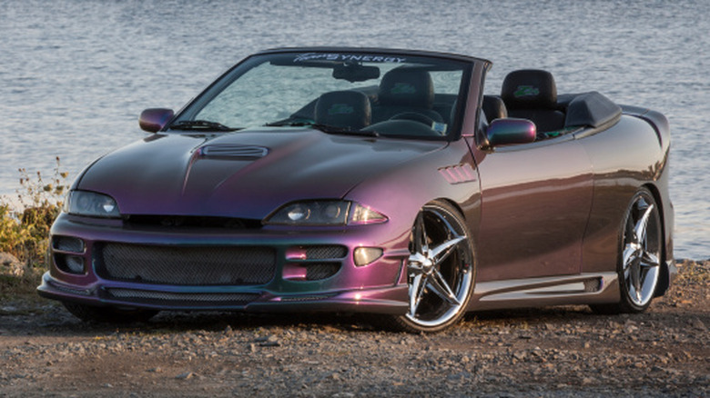 A heavily modified Chevrolet Cavalier convertible parked in front of a lake.