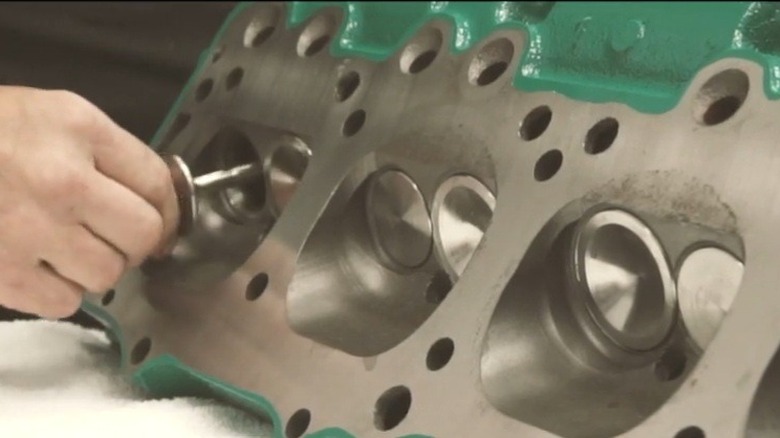 A man's hand places valves into a green-painted Buick Nailhead V8 head.