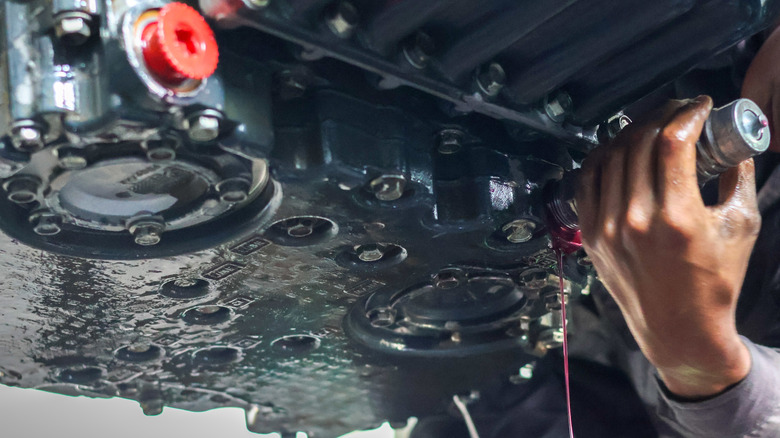 A mechanic loosening the ATF drain plug under a car