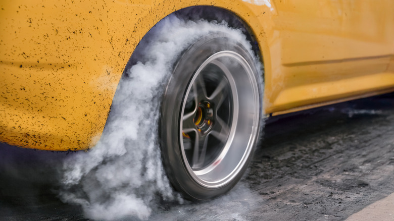 A close-up of a yellow car doing a burnout on a drag strip.