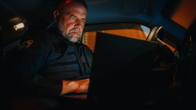 A stock image of a police officer or a security guard looking something up on a laptop in their cruiser.