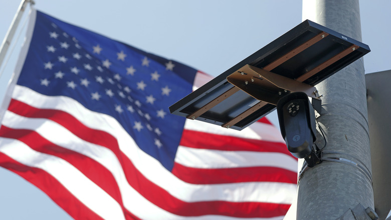 A Flock camera mounted on a pole in front of an American flag.