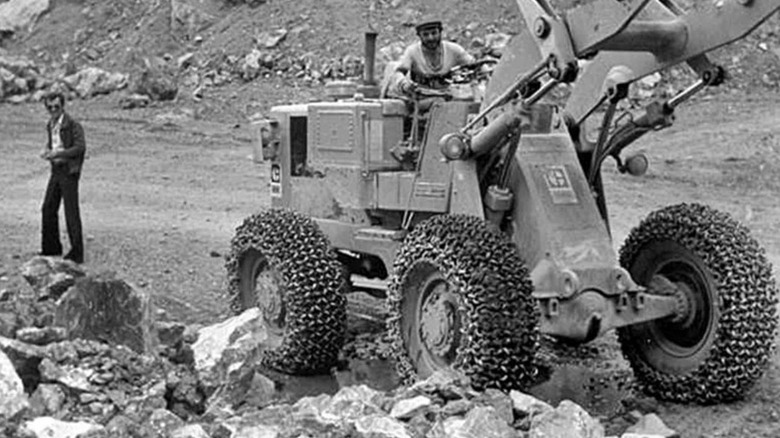 A black and white photo of an old industrial loader with tires wrapped in chains