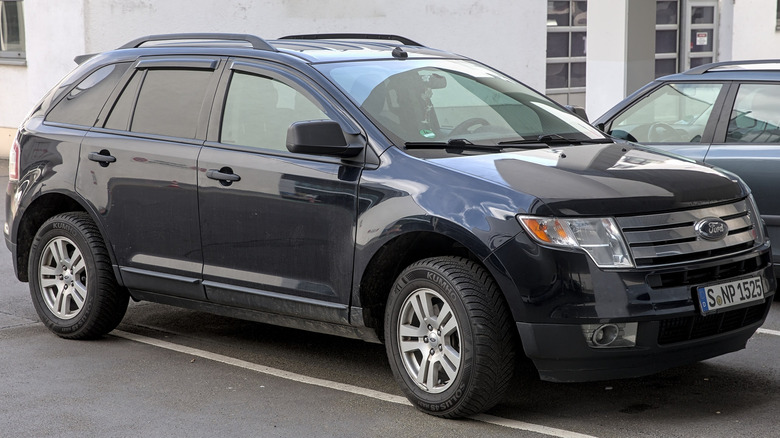 A black 2007 Ford Edge parked poorly in a parking lot with another vehicle and a building in the background.