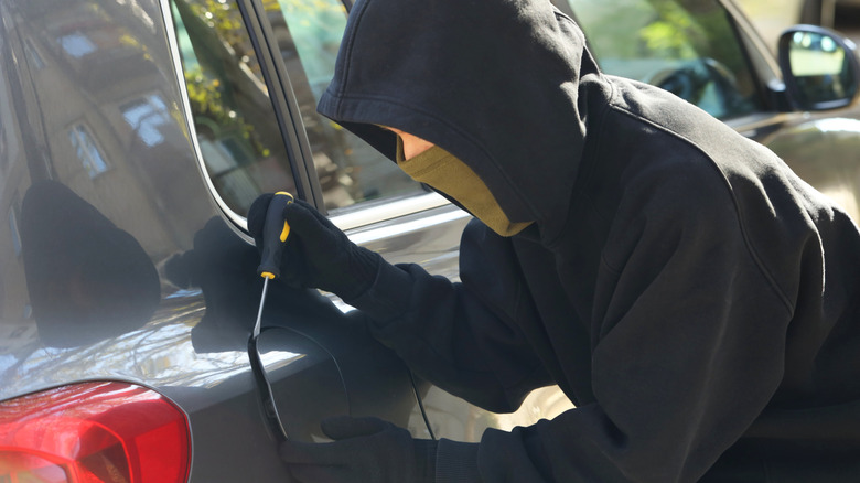 A thief trying to open a fuel door on a gray car