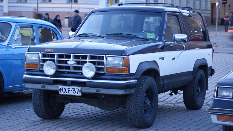 A black and white 1990 Ford Bronco II parked next to other cars.