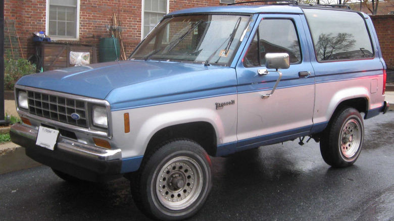 A silver and blue Ford Bronco II on a wet road.
