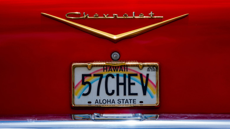 A Hawaii state license plate that reads "57CHEV" on the rear of a red 1957 Chevrolet.