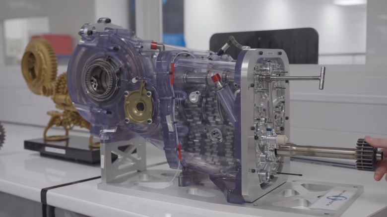 An F1 gearbox in a clear casing being inspected by a person offscreen