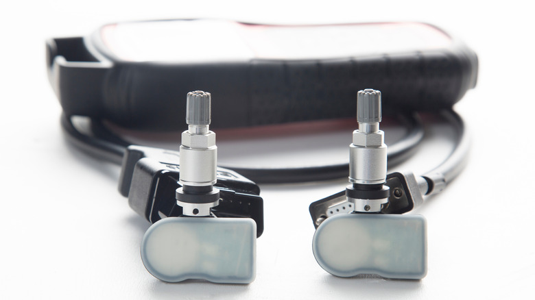 A set of two direct TPMS sensors with a programming tool in the background.