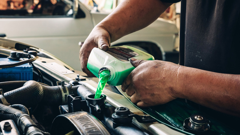Mechanic filling nan coolant reservoir successful a car.