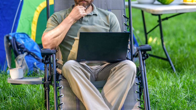 A man sitting in a camping chair in front of a tent and table with food