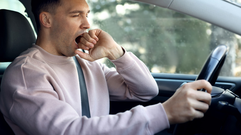 A man yawning while behind the wheel of a car