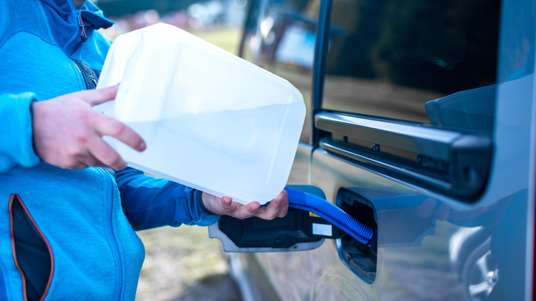 A driver adds DEF from a plastic jug to a blue vehicle