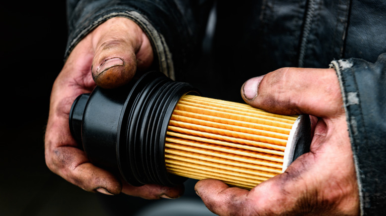 An oil filter being held by someone wtih dirty hands