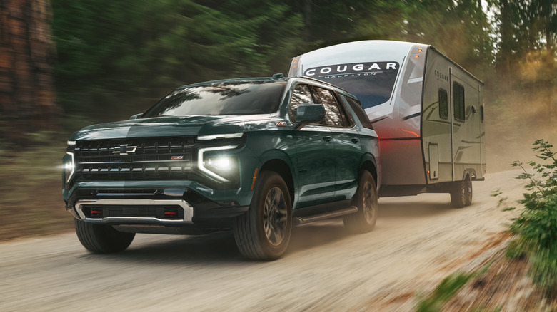 A green Chevy Tahoe towing a camper down a dirt road.