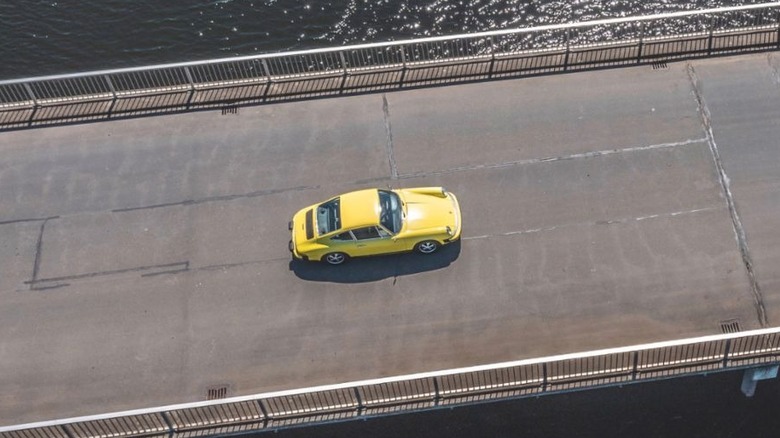 A yellow Porsche 912E prototype driving across a bridge