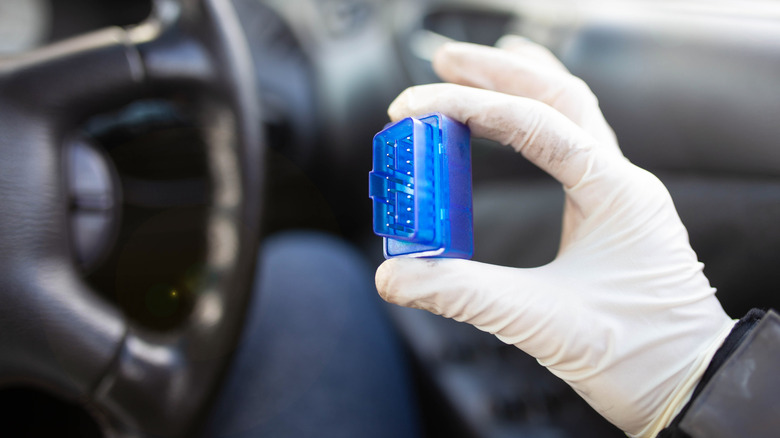 A technician holding a wireless OBD-II telemetry scanner, which syncs to a mobile device via Bluetooth.