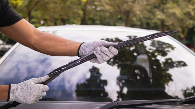 A person with gloved hands checking a wiper blade assembly.