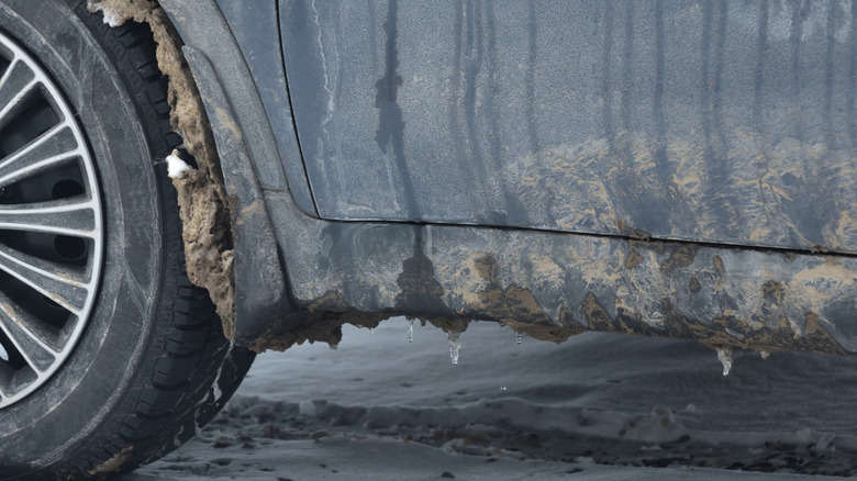 A dirty car with snow and ice in the wheel well and on the rocker panel.