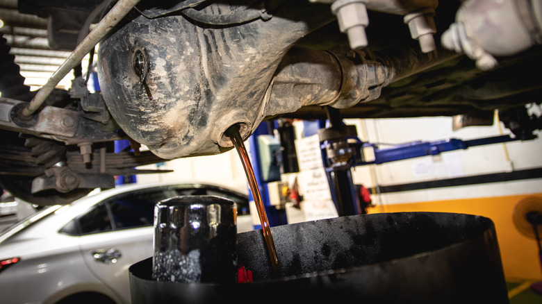 A differential draining fluid into a drain pan with an oil filter sticking out it, against a backdrop of a garage with silver parked car