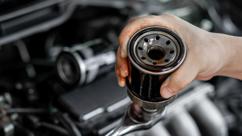 A person inspects an oil filter above an open engine bay