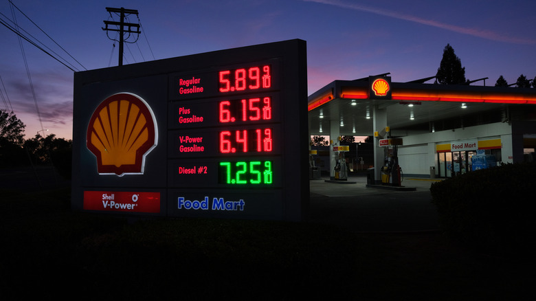 A Shell gas station sign displays high fuel prices at sunset