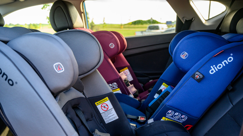 Three child seats, sitting in a row in a car's back seat.