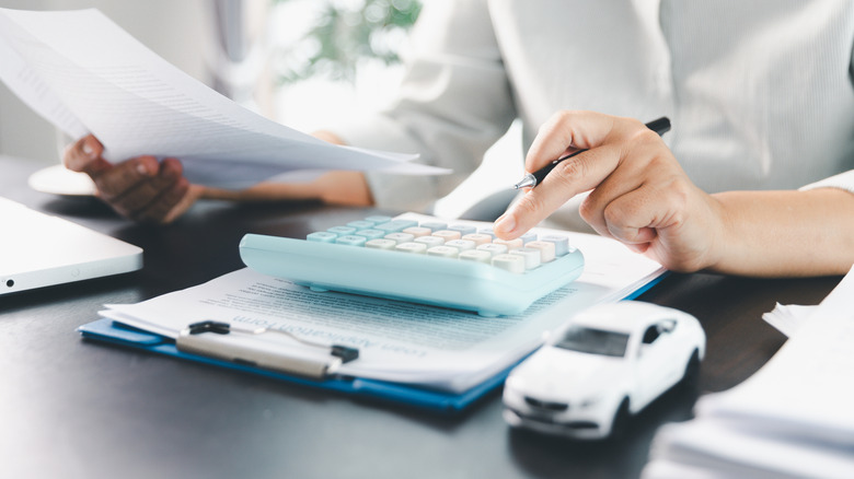 Osoba koja koristi kalkulator koji se nalazi na stolu pored bijelog autića.
