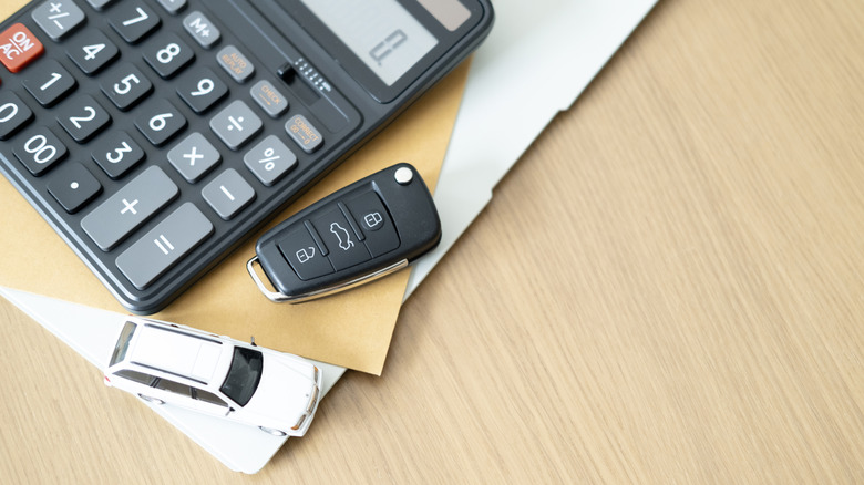 Kalkulator, ključ od automobila i bijeli autić na stolu.