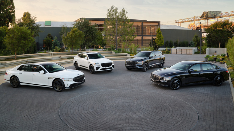 Genesis vehicles parked on a paved surface with a building and metal structures in the background