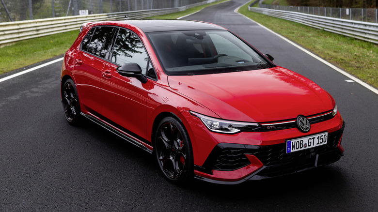 A red VW Golf GTI parked in the middle of a track with trees in the background.