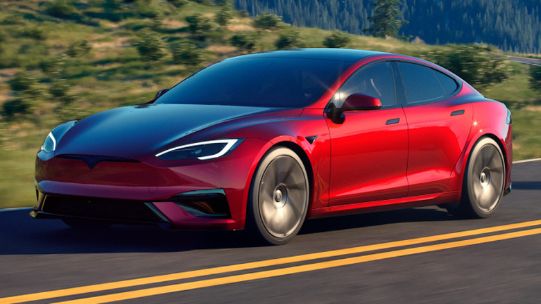 A red Tesla Model S driving around a corner on scenic mountain road