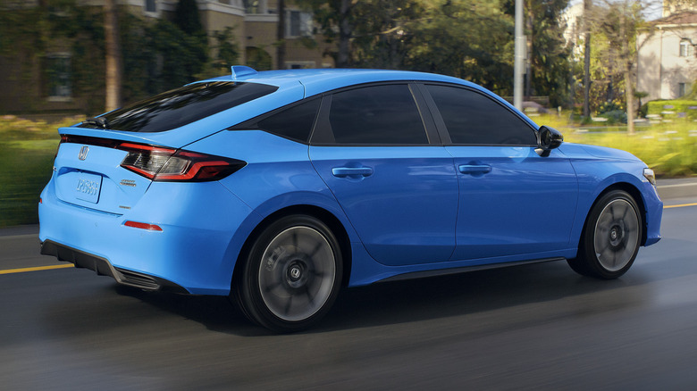 2025 Honda Civic Hatchback Sport Touring Hybrid driving down city street.