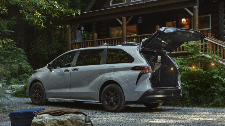 2026 Toyota Sienna Woodland parked on a gravel surface next to a cabin in a wooded area