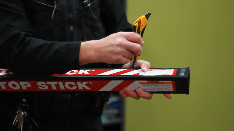 Police officer uses a utility knife to open the packaging of a black and red Stop Stick tire deflation device.