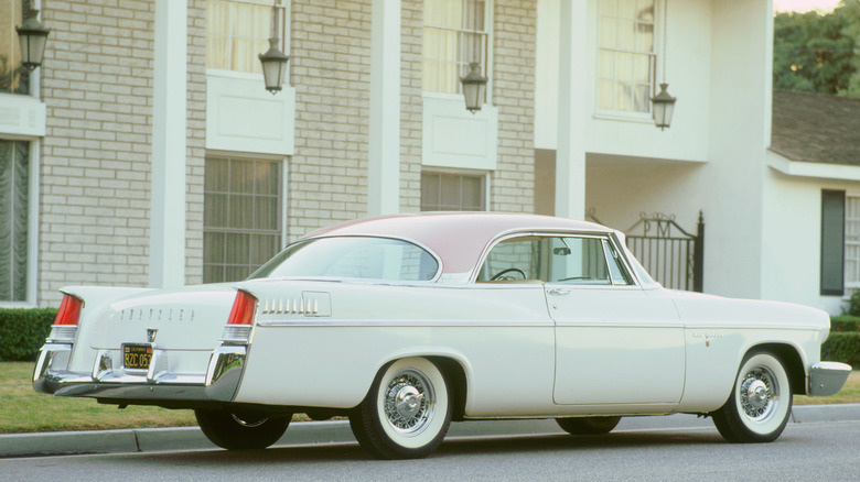 A white 1956 Chrysler New Yorker hangin' out parked in front of a large house, looking pretty.