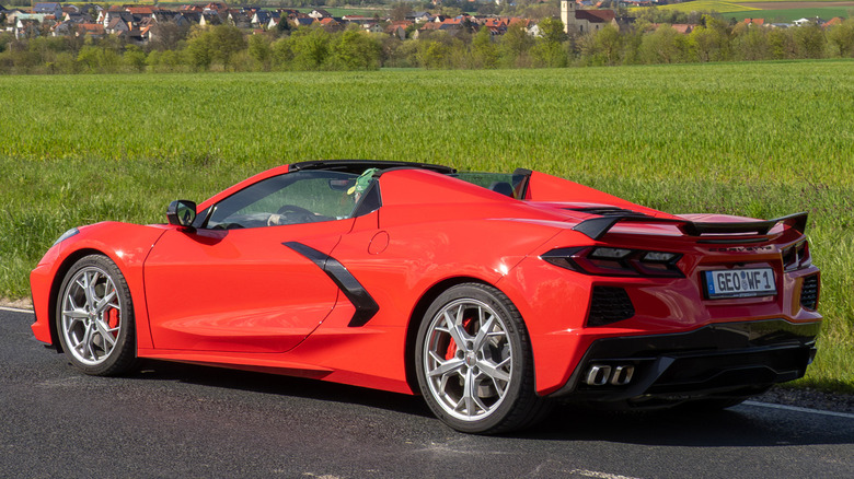 A red C8 Corvette parked on a rural road next to a green field.