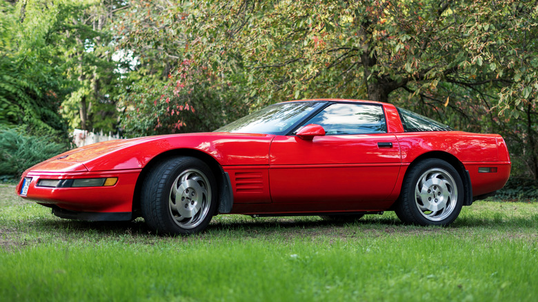 A red Corvette C4 sits parked on grass.