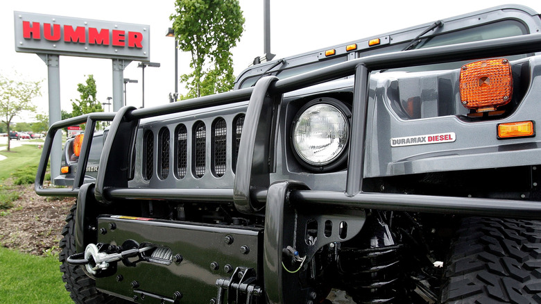 Close-up view of the front of a Hummer H1 with a "Hummer" dealer sign in the background