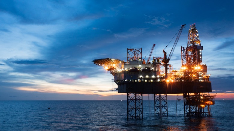 An off-shore oil rig sit against a calm blue sea and a distant sunset