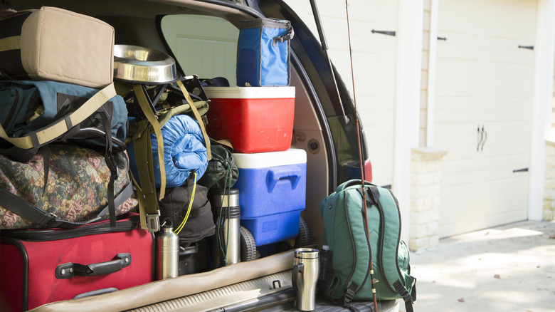 Thetrunk of a car fully packed with car camping gear, including coolers, backpacks, sleeping bags, thermos mugs, fishing gear, and more.