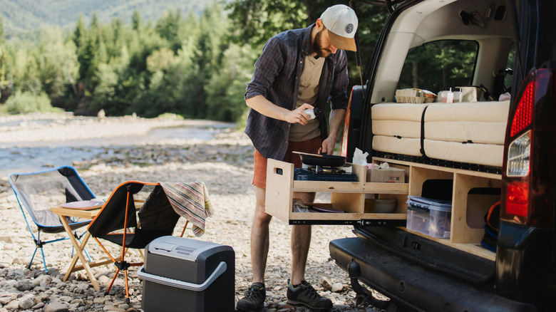 A young man neatly packing away camping gear in dedicated storage compartments under the bed in the trunk of his car.