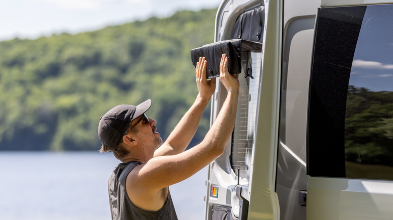 A man closing a privacy window shade installed on the window of a van.