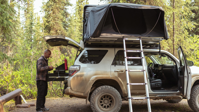 A man with a well-equipped car camping setup, including a rooftop tent and a fully functional kitchen in the trunk.