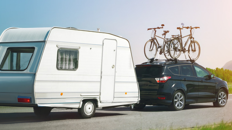 An SUV with bikes mounted on the roof towing a camper